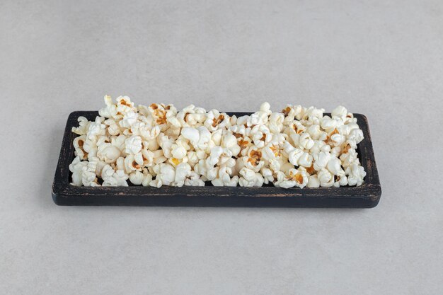 Black wooden tray with fresh popcorn on marble table.