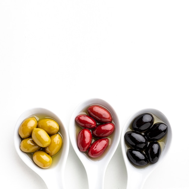 Black yellow red olives in spoons with copy space