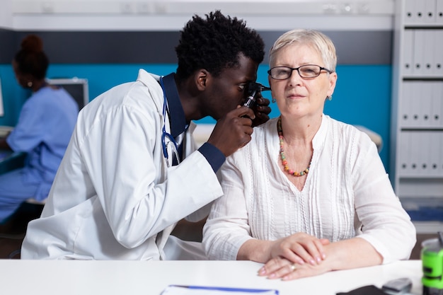 Black young doctor using otoscope on elder patient