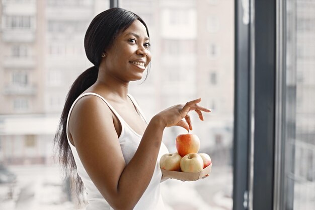 Black young woman in studio with big window holding apples