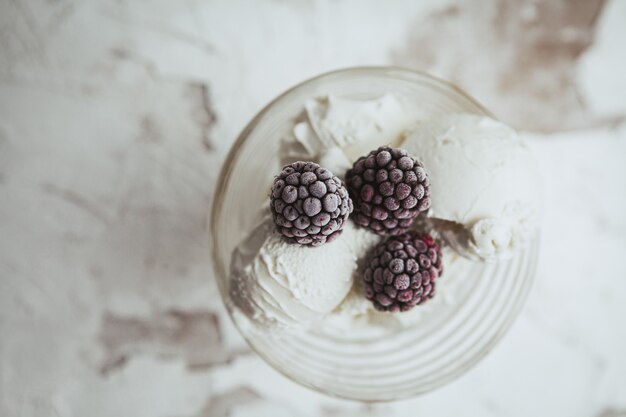 Blackberries in a glass cup with ice cream top view on a white textured