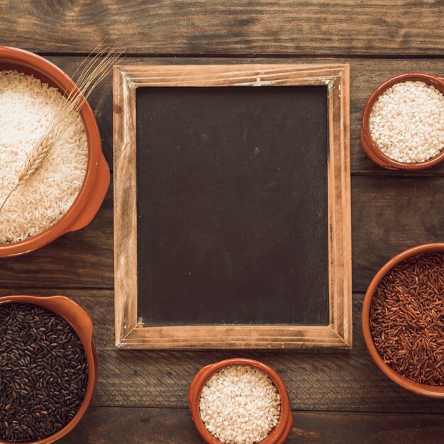 Blackboard frame with bowls of different rice on wooden table