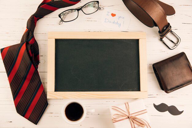 Blackboard among male accessories near gift and cup of drink