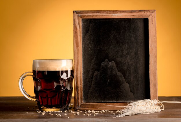 黒板に立っている次の木製のテーブルの上のビールのグラス