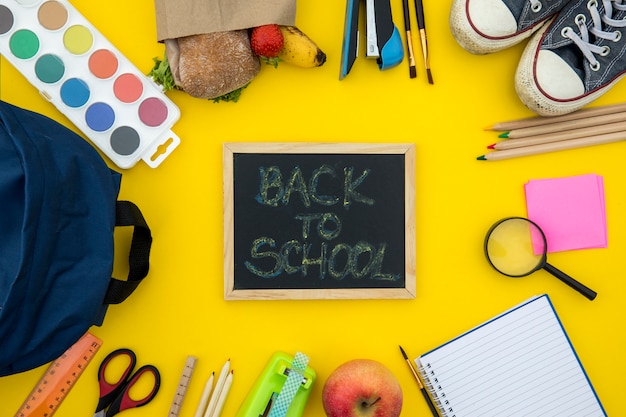 Blackboard with school accessories on yellow background