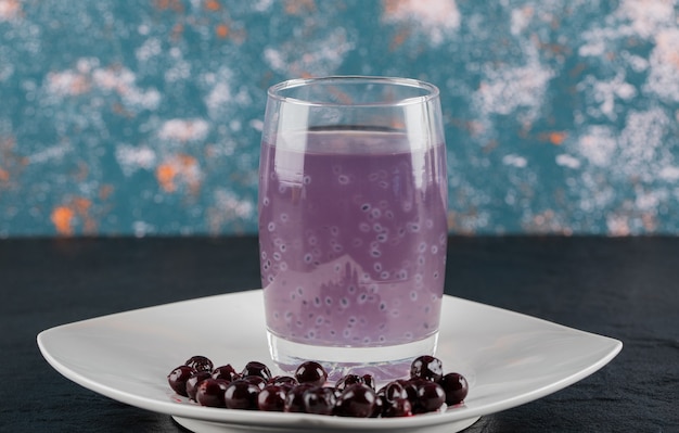Foto gratuita confettura di ribes nero in un piattino bianco con un bicchiere di succo intorno.
