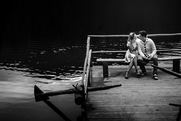 Blakc and white picture of young people kissing on bench over the lake
