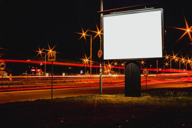 Blank advertisement billboard with blurred traffic lights at night