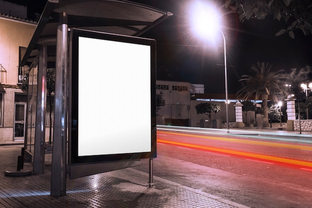Blank advertisement at bus shelter with blurred traffic lights at night