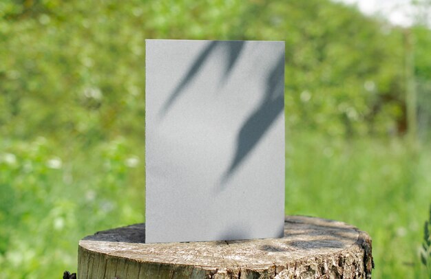 Blank bifold white card standing on wooden desk outdoor with floral shadow and blurred nature background