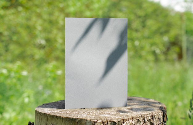 Blank bifold white card standing on wooden desk outdoor with floral shadow and blurred nature background