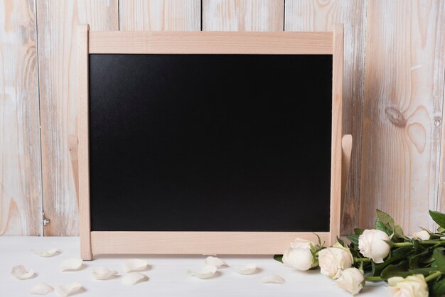 白い木製のテーブルに美しいバラと空の黒板