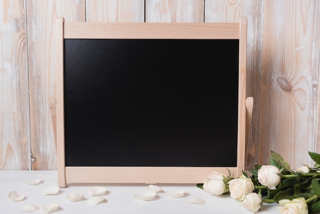 Blank blackboard with beautiful roses on white wooden table