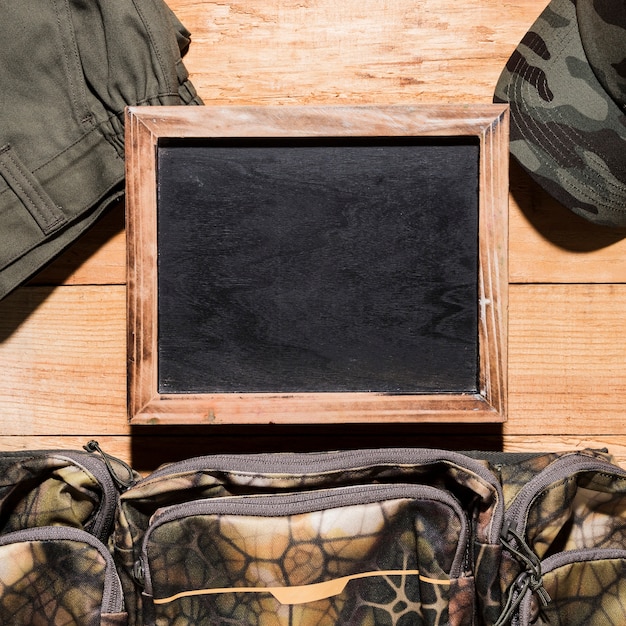 Blank blackboard with pants; bag and cap on wooden table