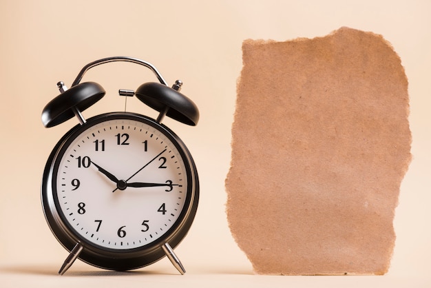 Blank brown torn paper near the black alarm clock against colored backdrop