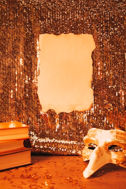 Blank burnt paper on shiny sequin fabric and party mask on desk