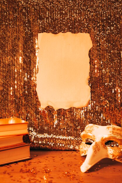 Blank burnt paper on shiny sequin fabric and party mask on desk