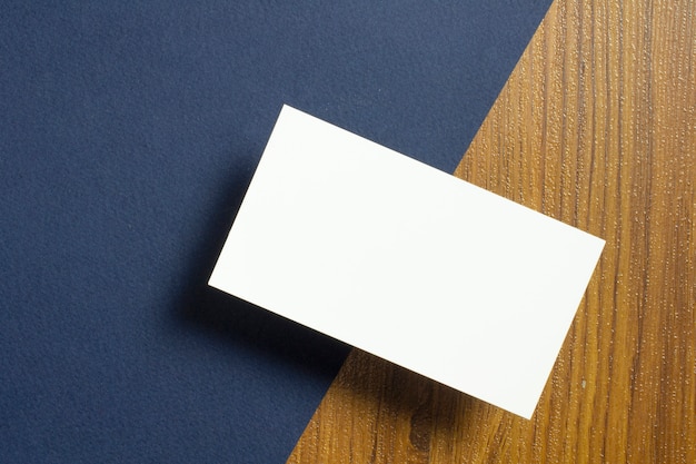 Blank business cards half of each lie down on blue textured  paper and wooden desk