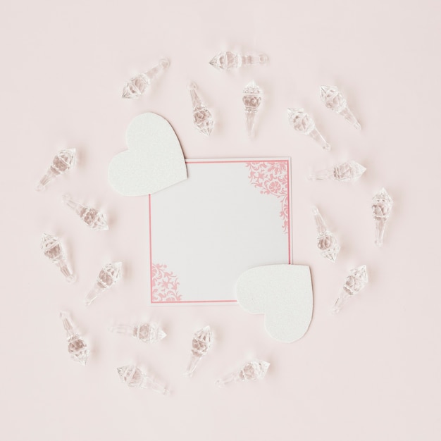 Пустая карточка и форма сердца в окружении хрустальных раковин на розовом фоне