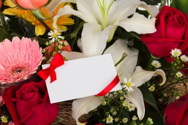 Blank card with red ribbon over flowers