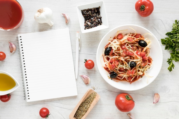 Blank diary and yummy spaghetti pasta with fresh ingredient on white wooden table