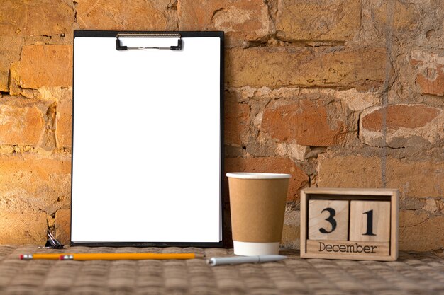 blank empty clipboard on the brown brick wall with coffee cup and pencils. Copyspace, 31 of December, new years resolutions.
