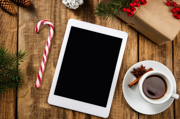 Пустой пустой экран планшета на деревянной стене с красочными праздничными украшениями, чаем и подарками.