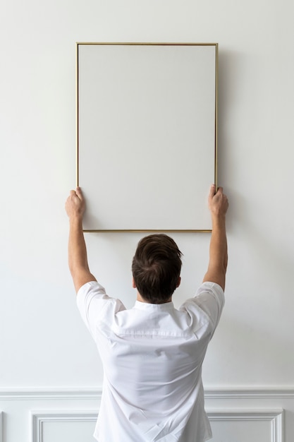 Бесплатное фото Пустая рамка, которую молодой человек вешает на белой минимальной стене