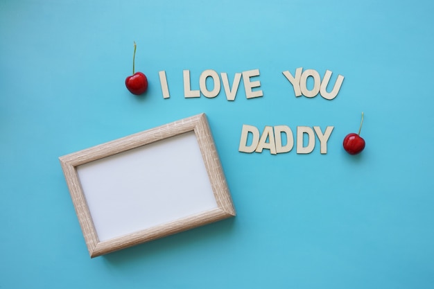 Blank frame and cherries on blue surface for father's day