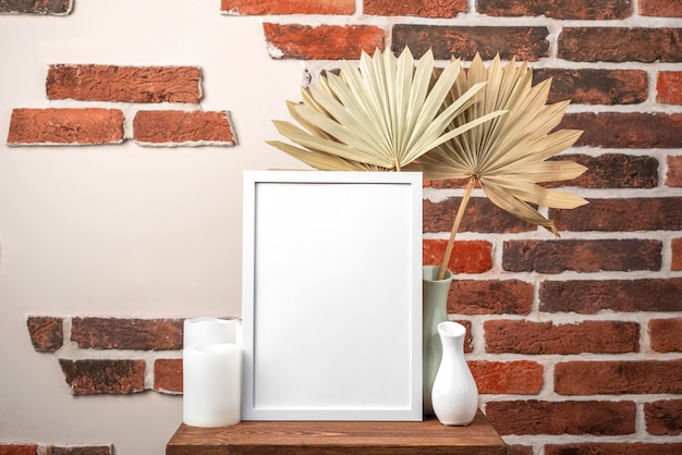 Blank frame on shelf beside vase with dry leaves