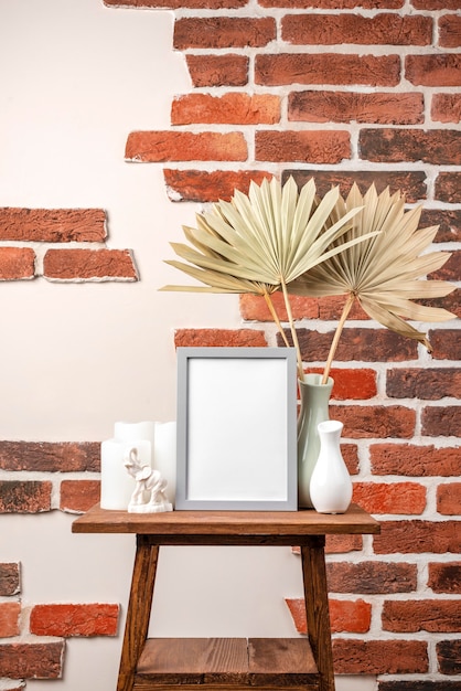 Blank frame on shelf beside vase with dry leaves
