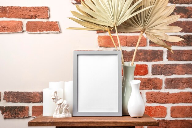 Blank frame on shelf beside vase with dry leaves