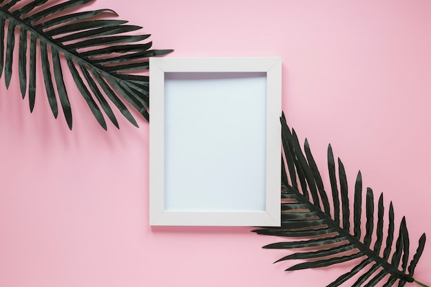 Free photo blank frame with green leaves on table