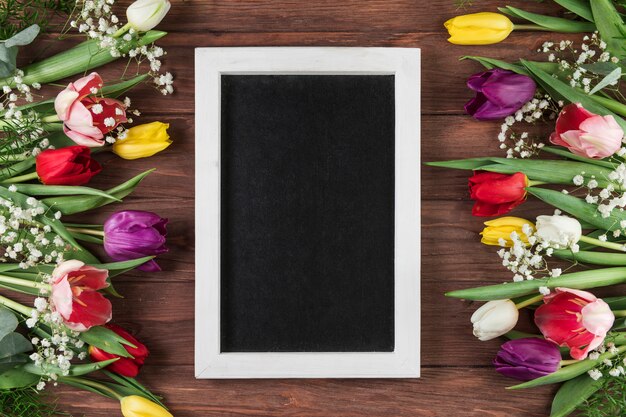 Blank frame with white border between the colorful tulips and baby's breath flower on wooden desk