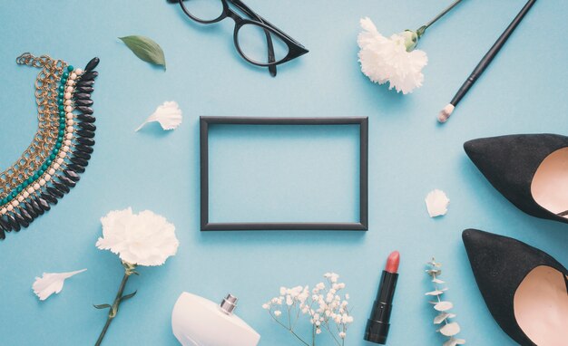 Blank frame with white flowers, woman shoes and cosmetics