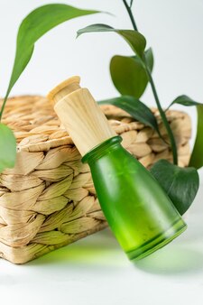 Blank green frosted glass essential oil bottle with pipette on beige background decorated green leaves. skin care concept with natural cosmetics.