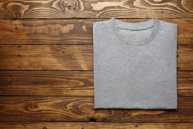 Blank grey t-shirt accurately folded on rustic wooden table top view 