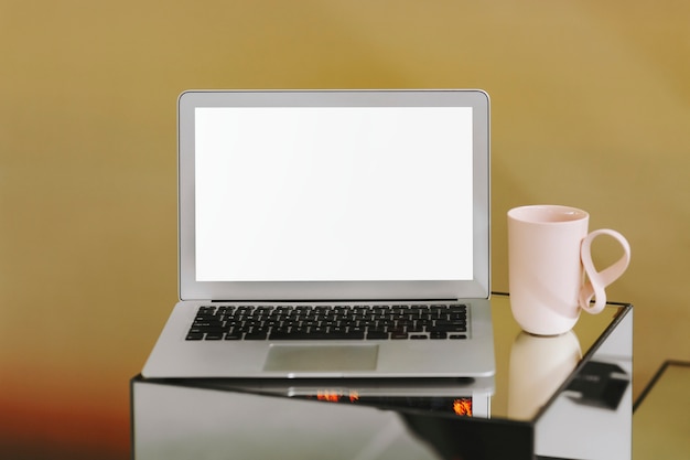 Schermo del computer portatile in bianco e una tazza di caffè rosa