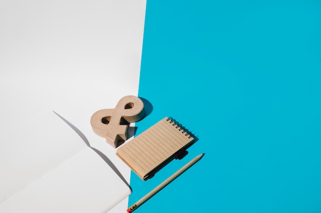 Бесплатное фото Пустой ноутбук; символ амперсанда; карандаш; и спиральный блокнот на двойных обоях