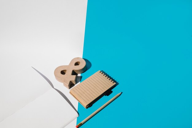 Пустой ноутбук; символ амперсанда; карандаш; и спиральный блокнот на двойных обоях