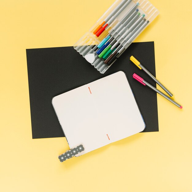 Blank notebook and colorful felt-tip pens on black and yellow card paper background