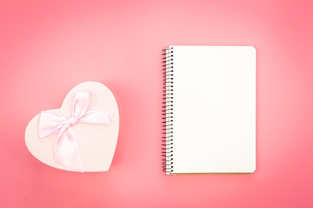 Free photo blank notebook and heart shaped gift box on pink background top view