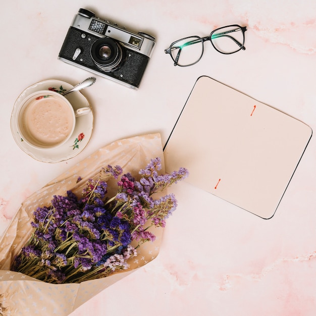 Foto gratuita taccuino in bianco con tazza di caffè, macchina fotografica e bicchieri sul tavolo