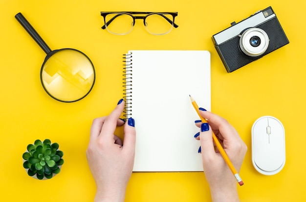 Blank notepad in female hands on a yellow background flat lay