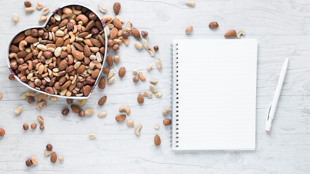 Blank notepad and pen with dryfruits in heart shape on wooden desk