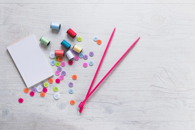 Blank notepad with spools; buttons and knitted needles on textured background