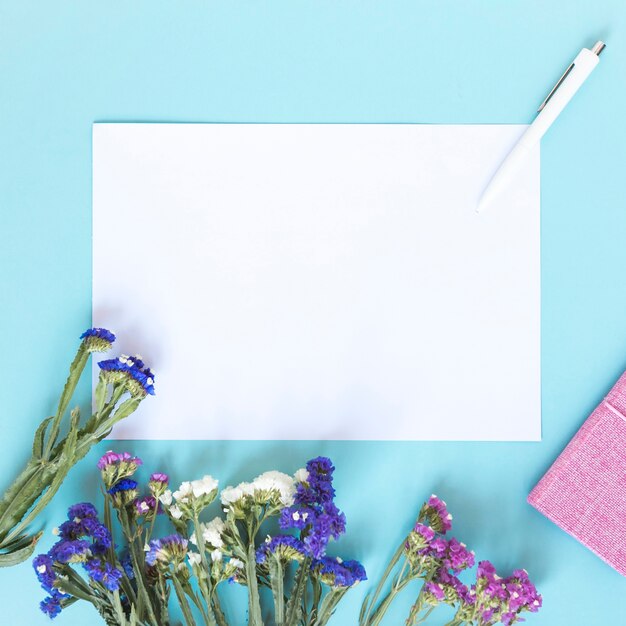 Blank paper sheet; pen and bunch of colorful flowers on blue backdrop