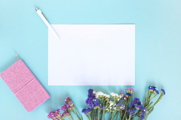 Blank paper sheet; pen; diary and bunch of flowers on blue backdrop