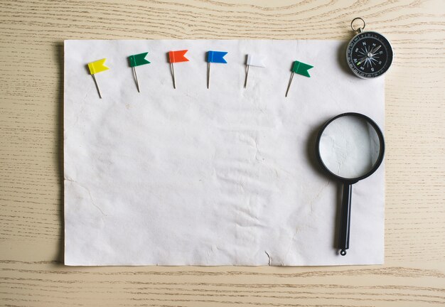 Чистый лист бумаги с цветными указателями, компас и увеличительное стекло
