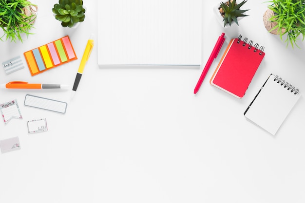 Blank paper with office supplies and plant pots on white backdrop